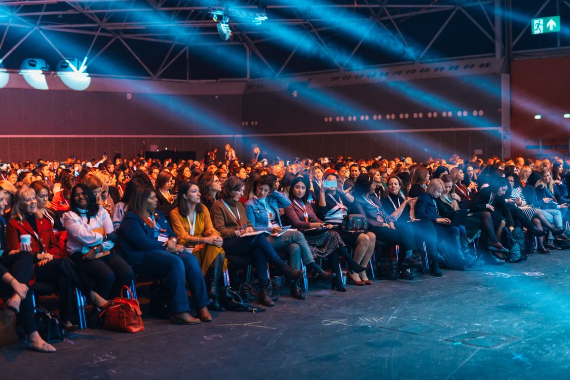 Auditorio lleno de mujeres durante una conferencia, con iluminación de escenario. Fotografía de referencia.